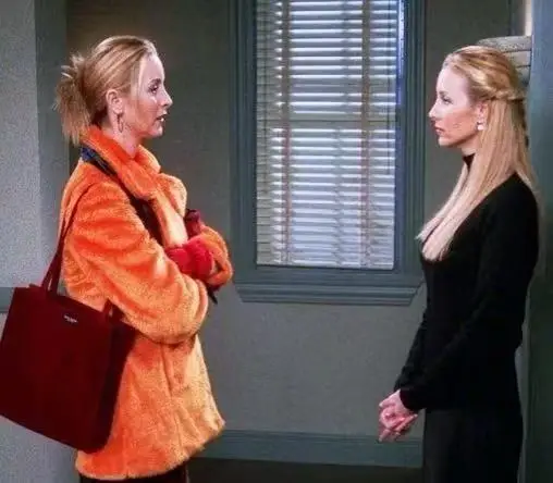 Twin sisters Phoebe Buffay and Ursula from Old Friends reunite in the hallway, with Phoebe on the left in an orange jacket and Ursula on the right in a black top.